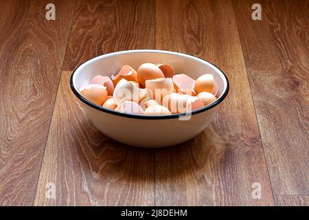 an iron bowl with eggshells stands on a wooden table top of a brown table, the remains of used chicken eggs are broken cracked shells. Stock Photo