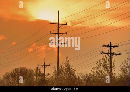 Geneva, Illinois, USA. Telephone poles and lines front a color display in the clouds shortly before sunset on a spring evening. Stock Photo