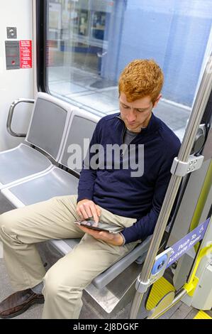 A young man with red hair using a electronic communication  device while using public transit Stock Photo