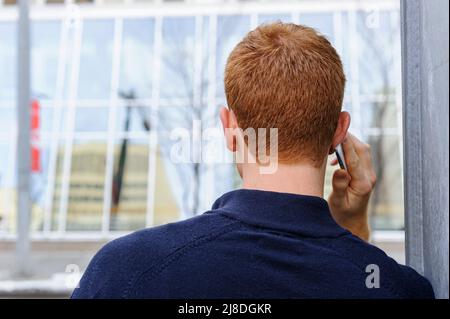 A young man with red hair using a electronic communication device mobile phone or cell phone Stock Photo