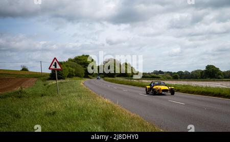 A yellow Caterham 7 (Lotus 7) sports car drives on a sunny day along the the English countryside A272 road. Stock Photo