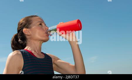 Sporty woman drinking water from a bottle on a hot day, re hydrating. Stock Photo