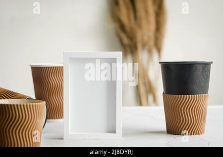 Empty white frame and many different craft paper disposable cups. Set of craft paper cups for coffee or tea on grey background. Zero waste, plastic fr Stock Photo