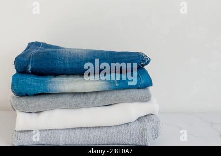 Stack of sweaters  and  blue jeans on grey background, ironing, laundry, home comfort, textile, knitted, women's clothing, cotton, women's casual all- Stock Photo