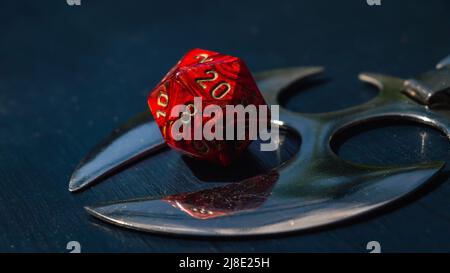 Close-up image of a red 20-sided role-playing die and a shiny object Stock Photo
