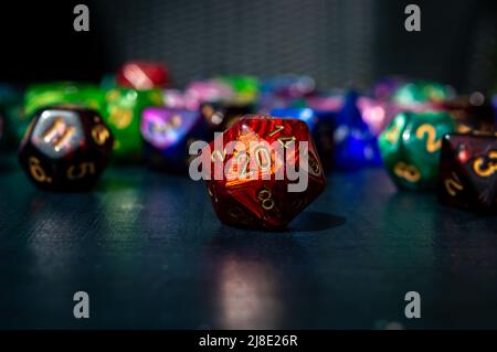 Close-up image of a red 20-sided role-playing die. In the background are various colored polyhedral dice Stock Photo