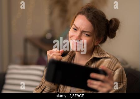 A pretty blonde girl plays a video game on a portable game console. A tense moment, the girl emotionally reacts to the game. New modern technologies, Stock Photo