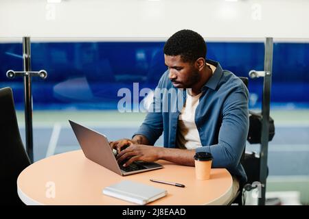 Vibrant portrait of handsome black man using laptop in sports training center, copy space Stock Photo