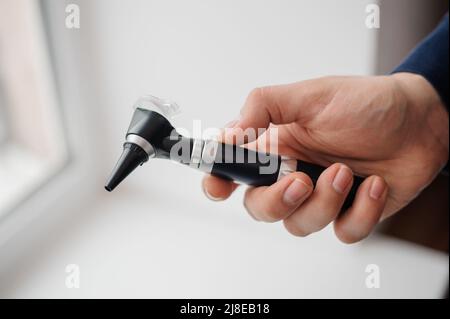 Otoscope on a white background in the hand of an otolaryngologist. Instrument for examining the auricle and middle ear Stock Photo