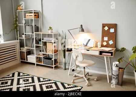 Cozy home office interior in minimal white color with focus on wooden desk lit by lamplight, copy space Stock Photo
