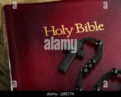 Macro shot. Red Book - Holy Bible and black Catholic cross on the rosary. Symbols of Christianity, Catholicism. Faith, spirituality, love, forgiveness Stock Photo