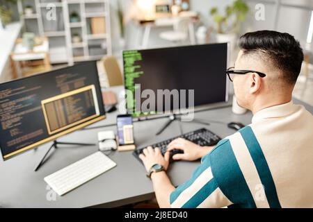 High angle view at Asian IT developer typing on keyboard with programming code on computer screen while working in office interior, copy space Stock Photo