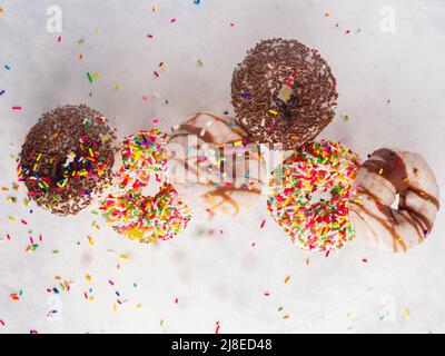 Multi-colored donuts covered with sugar icing, confectionery sprinkles and chocolate in a frozen flight on a white background. Holiday, birthday. Swee Stock Photo