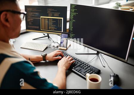 Closeup of IT developer typing on keyboard with programming code on computer screen while working in office interior, copy space Stock Photo