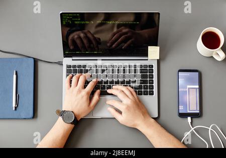 Minimal top view of unrecognizable man using laptop and writing code at grey workplace desk Stock Photo