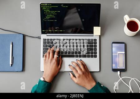 Minimal top view of unrecognizable black woman using laptop and writing code at grey workplace desk Stock Photo