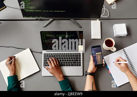 Minimal top view of QA engineers using laptop and reviewing code at grey workplace desk Stock Photo