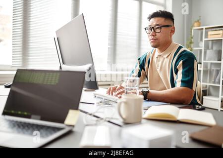 Portrait of Asian software developer using laptop while working at desk in office setting, copy space Stock Photo