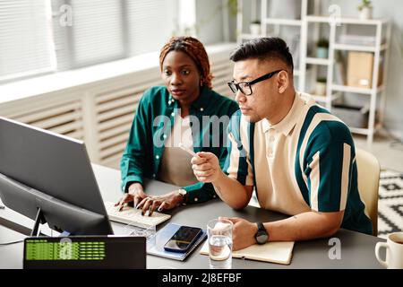Portrait of diverse software development team using laptop while working at desk in office setting Stock Photo
