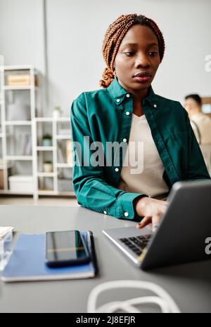 Vertical portrait of black young woman using laptop while working at desk in software development studio Stock Photo