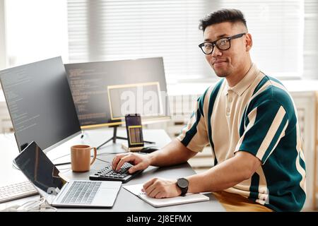 Warm toned portrait of Asian IT developer or QA engineer looking at camera while sitting at workplace with computers, copy space Stock Photo
