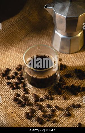 A transparent glass cup with coffee and a geyser coffee maker on a dark burlap background with coffee beans. View from above Stock Photo