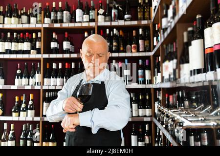 senior man professional sommelier tasting red wines in wine store Stock Photo