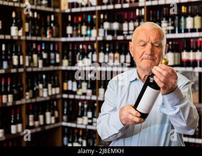 Elderly man chooses red wine in a liquor store Stock Photo