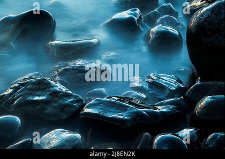 The silky appearance of the water lapping around the smooth boulders on the rocky shore of Fair Isle. A long exposure with a neutral density filter Stock Photo