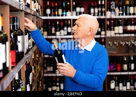 Attentive pensioner chooses red wine in a liquor store Stock Photo