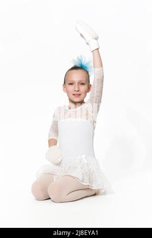 Caucasian girl ballet dancer in white ballet tutu skirt sitting on white floor. Studio shot. Part of photo series Stock Photo