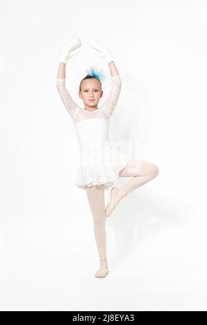 Caucasian girl ballet dancer in white ballet tutu skirt, blue bow in hair and white mittens posing on white background with shadow. Full length Stock Photo