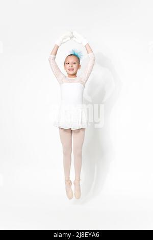 Girl ballerina in white ballet tutu skirt, blue bow in hair and white mittens dancing on white background with shadow. Full length, studio shot Stock Photo