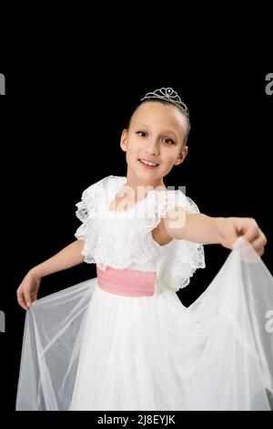 Smiling girl ballet dancer with diadem on head dressed in white long dress dancing on black background in studio. Caucasian ballerina nine-year-old Stock Photo