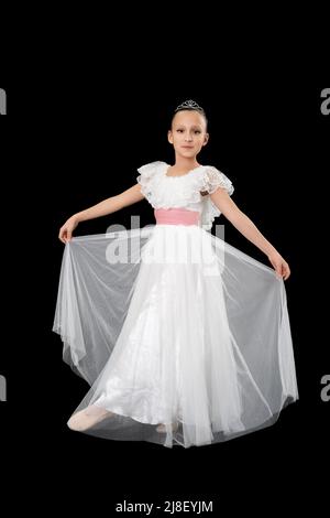 Girl ballet dancer nine-year-old in white long dress posing on black background. Full length, studio shot. Part of photo series Stock Photo
