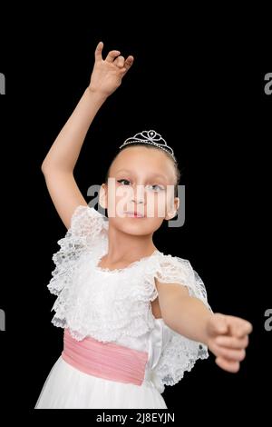 Cute girl ballerina in white long dress dancing on black background. Caucasian ballet dancer nine-year-old posing and looking at camera. Waist up Stock Photo