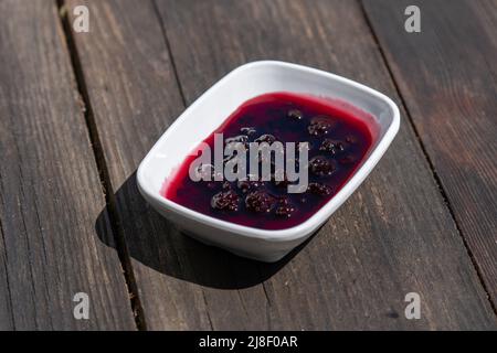 Selective focus down view of plate of blackberry jam on wooden table. Stock Photo