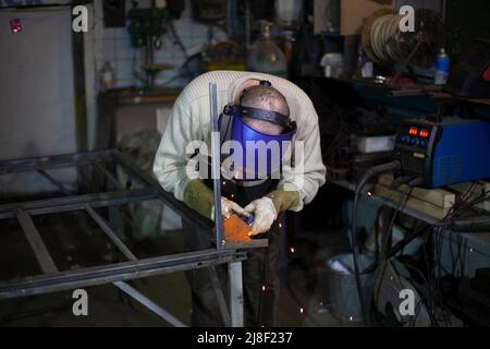 Welder at work. The welder heats the metal. Classes in the workshop. Steel processing. Welder in a blue welding mask. High melting point of metal. A m Stock Photo