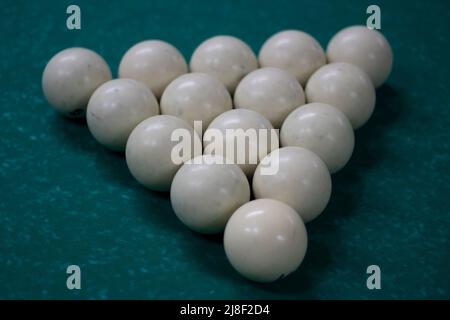 Billiard balls are collected in triangle. White balls on pool table. Details of sports equipment. Green cloth on table. Preparation of game. Stock Photo