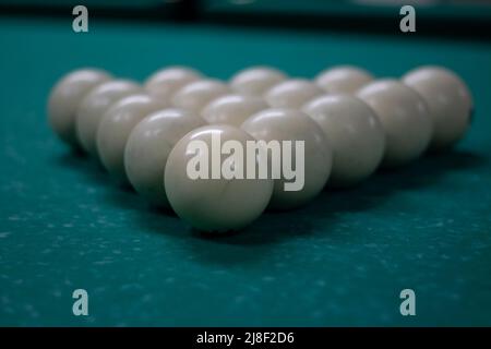 Billiard balls are collected in triangle. White balls on pool table. Details of sports equipment. Green cloth on table. Preparation of game. Stock Photo