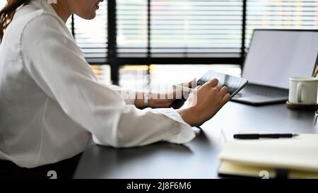 Asian working woman sitting at her office desk, using digital tablet touchpad, planning her meeting schedule. rear view, cropped image Stock Photo