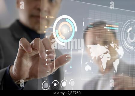 Two Asian businessmen interacting with futuristic virtual touchscreen while analysing business information data Stock Photo