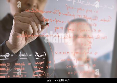 Asian businessmen writing finance equations on glass wall of a meeting room while disscuss the his co-worker Stock Photo