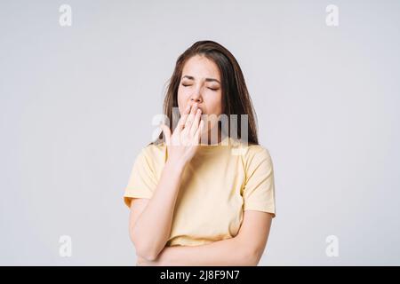Young yawning asian woman winner with long hair in yellow shirt on grey background Stock Photo