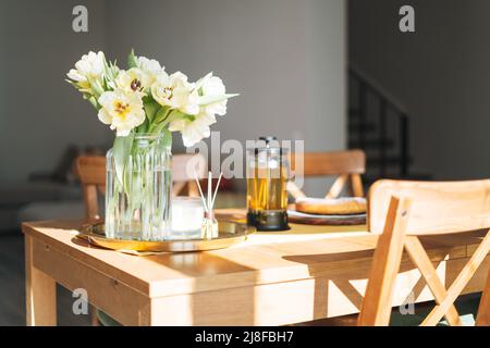 Beautiful bouquet of yellow tulips in vase on dinner table in white kitchen light interior at home Stock Photo