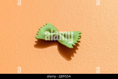 Single ribbon-shaped pasta isolated on orange background in bright light. Spinach pasta in the shape of a bow tie, minimalist on a colorful table. Stock Photo