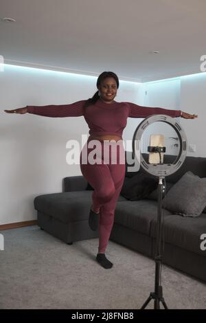 African young woman doing yoga virtual fitness class with her phone at home. Stock Photo