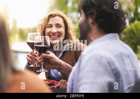 Happy couple of 40s people having fun toasting outdoors sitting at the barbecue table - lifestyle conviviality concept - forty-year-olds at the table Stock Photo