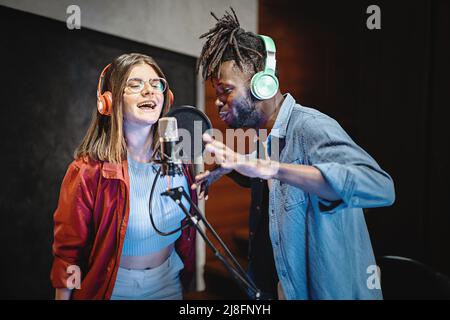Couple of young people performing a vocal live session online streaming by the internet - multiethnic people having fun singing around the microphone Stock Photo