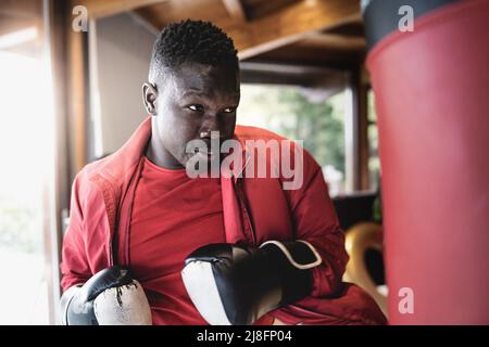 A young man of African ethnicity punches the punching bag while wearing gloves - lifestyle concept of young people practicing sport Stock Photo